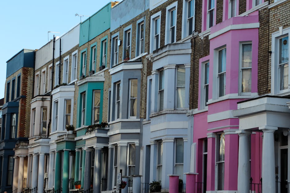 A row of terraced houses on Portobello Road in Notting Hill, W11, featuring colourful facades in shades of teal, white, blue, and pink. Each house has large, double-glazed sash windows, some with flow